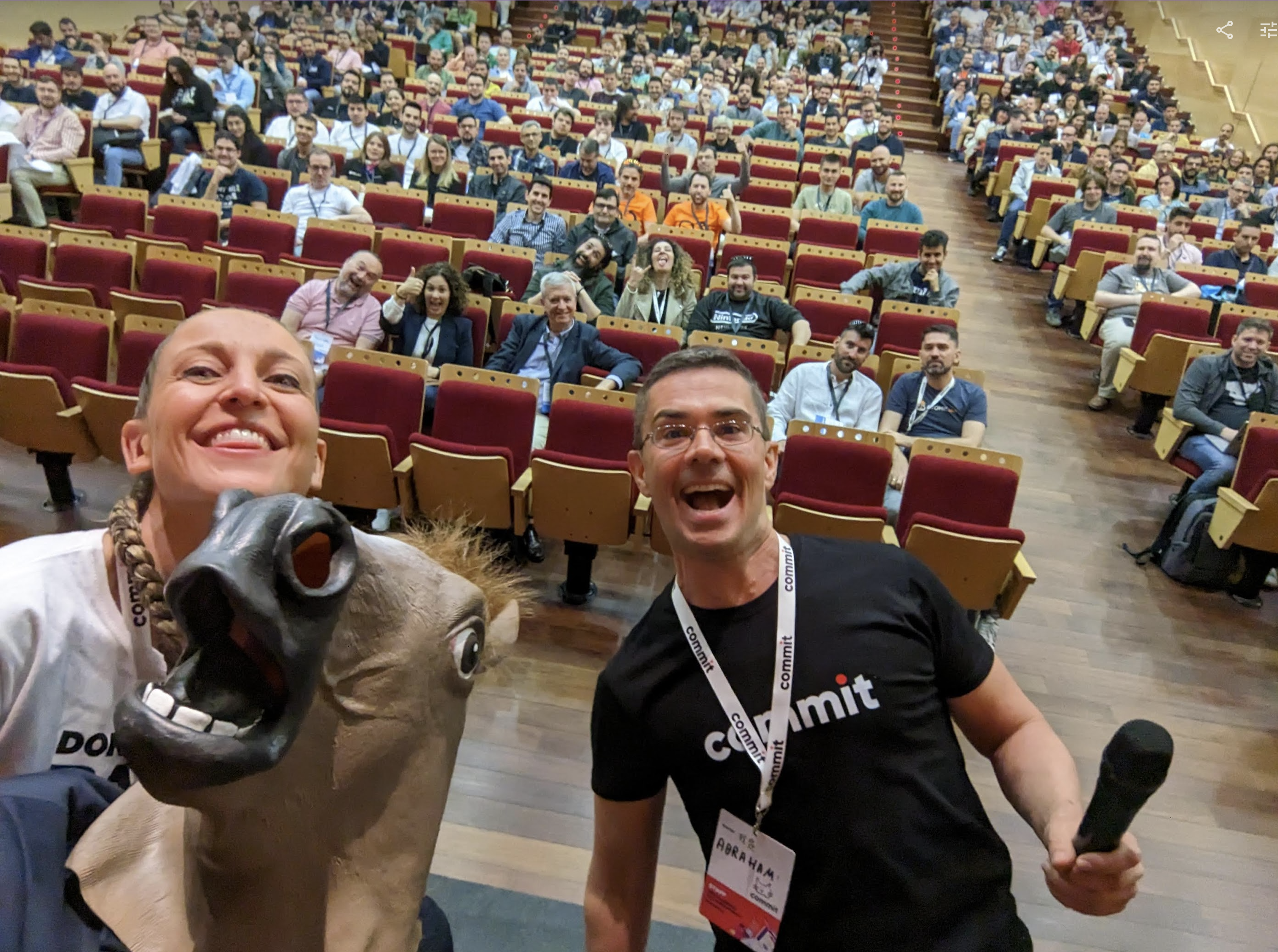 A selfie taken during the keynote, with the auditorium two thirds full of people and Laura, Abraham and Nacho on stage, smiling. Nacho is wearing a horse mask, but under that, there is a smile too.